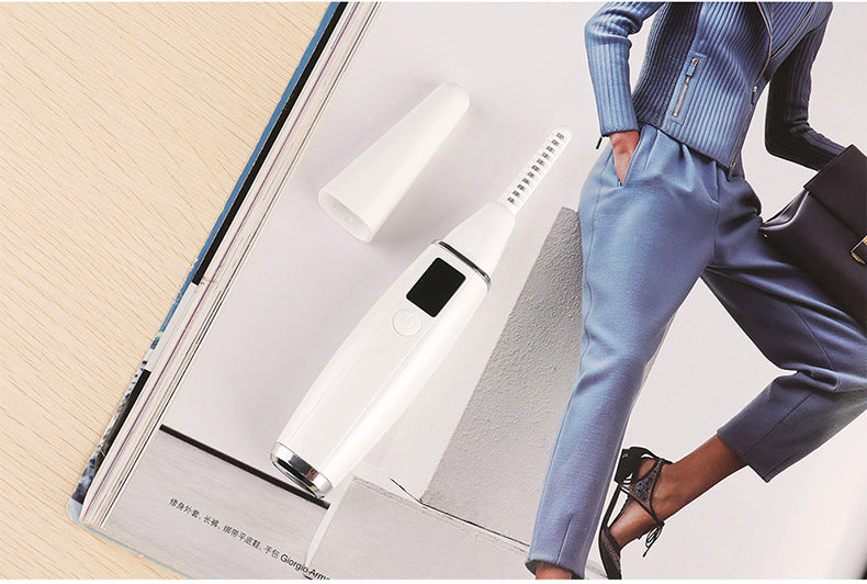 White heated eyelash curler with protective cap placed on top of a fashion magazine.