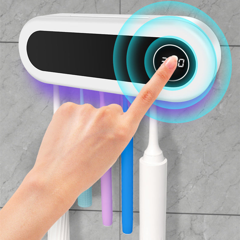 Hand pressing a touch-activated button on a wall-mounted mop and broom holder with hanging cleaning tools.