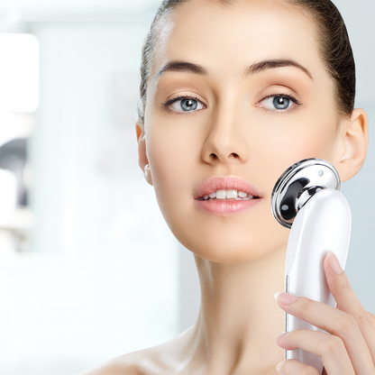 Woman using a white handheld facial massager on her cheek for skin care treatment