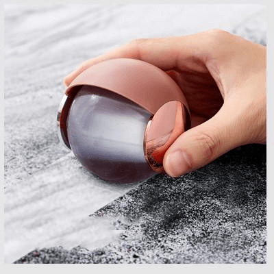 Hand using rose gold and grey reusable lint remover on textured fabric surface